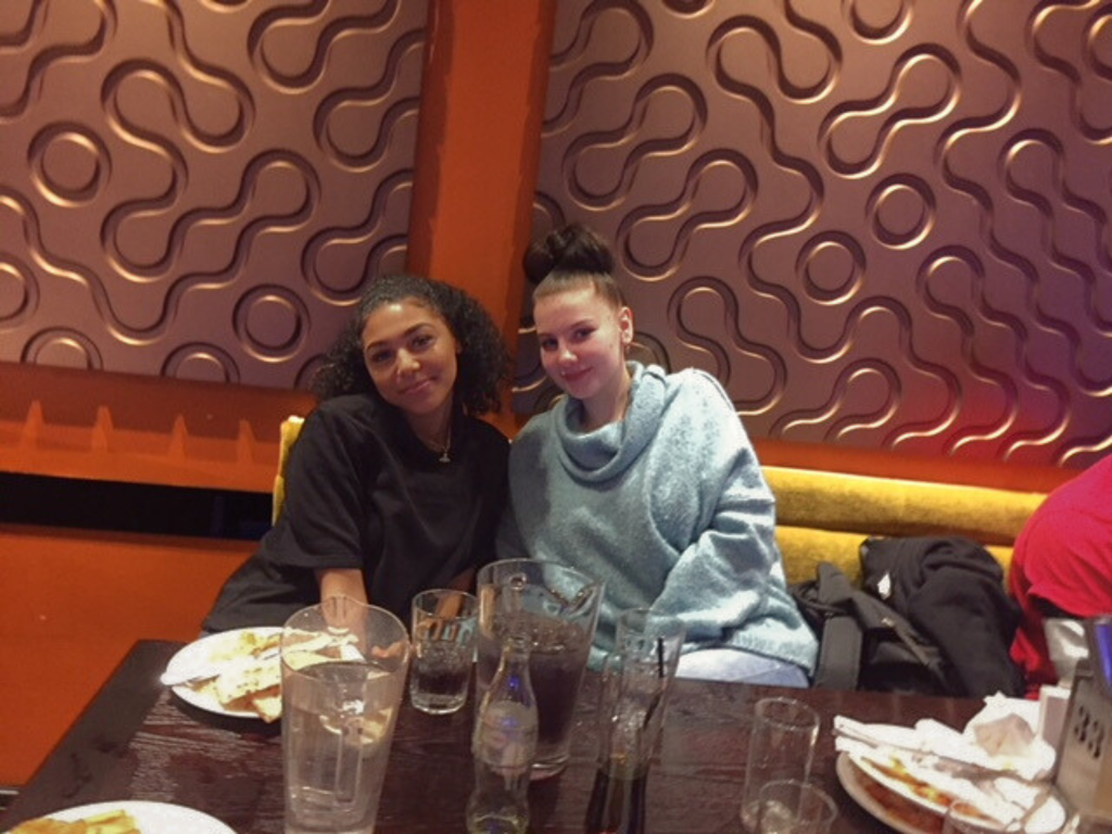 A photo of two past clients, both women are leaning in and smiling at the camera, they are in a restaurant booth with empty plates and glasses in front of them